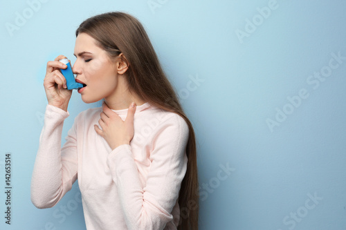 Young woman using asthma inhaler on color background photo