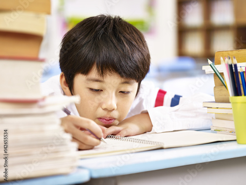 Cuadro en lienzo tired and bored asian schoolboy doing homework in classroom