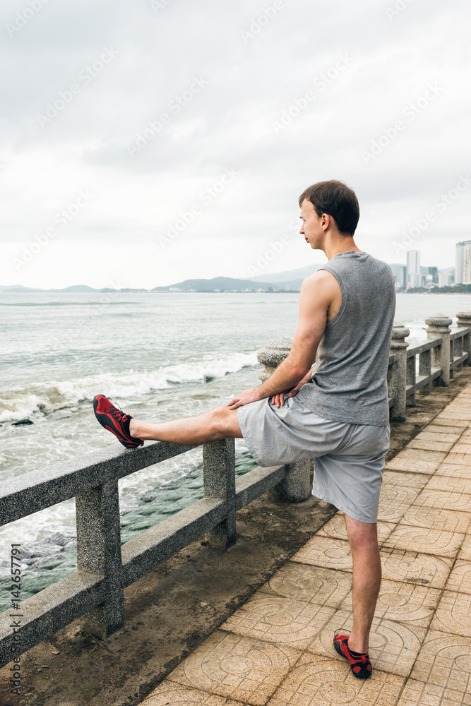 Man stretching before jogging on the embankment. Athletic runner doing stretching exercise, preparing for morning workout Man stretching before jogging on the embankment. Athletic runner doing stretching exercise, preparing for morning workout