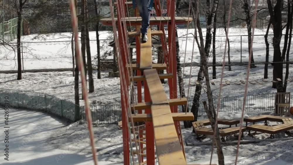 Young female climber walks by pendant log bridge on high ropes course in extreme park Young female climber walks by pendant log bridge on high ropes course in extreme park