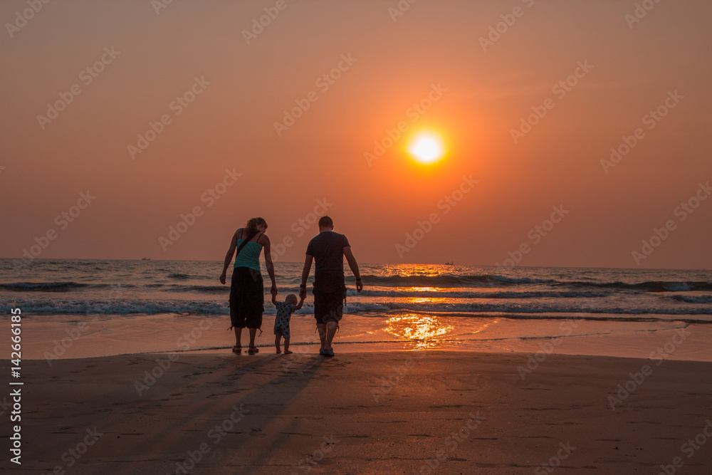 Happy family together, parents with their little child at sunset. Arambol beach, North Goa, India