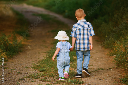 children walk in the Park , the older brother holds his sister's hand