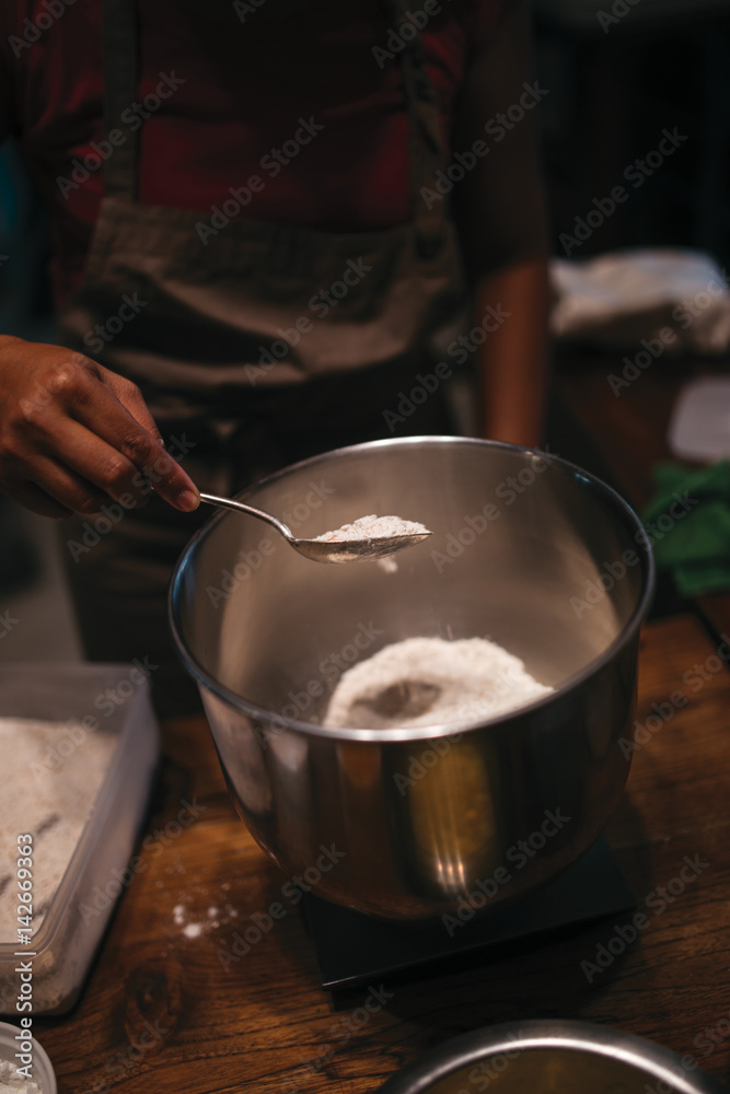 Close up of woman hands who spoons a flour into the metal bowl Close up of woman hands who spoons a flour into the metal bowl