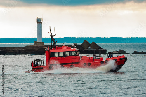 Red pilot ship sailing to Baltic sea past the lighthouse