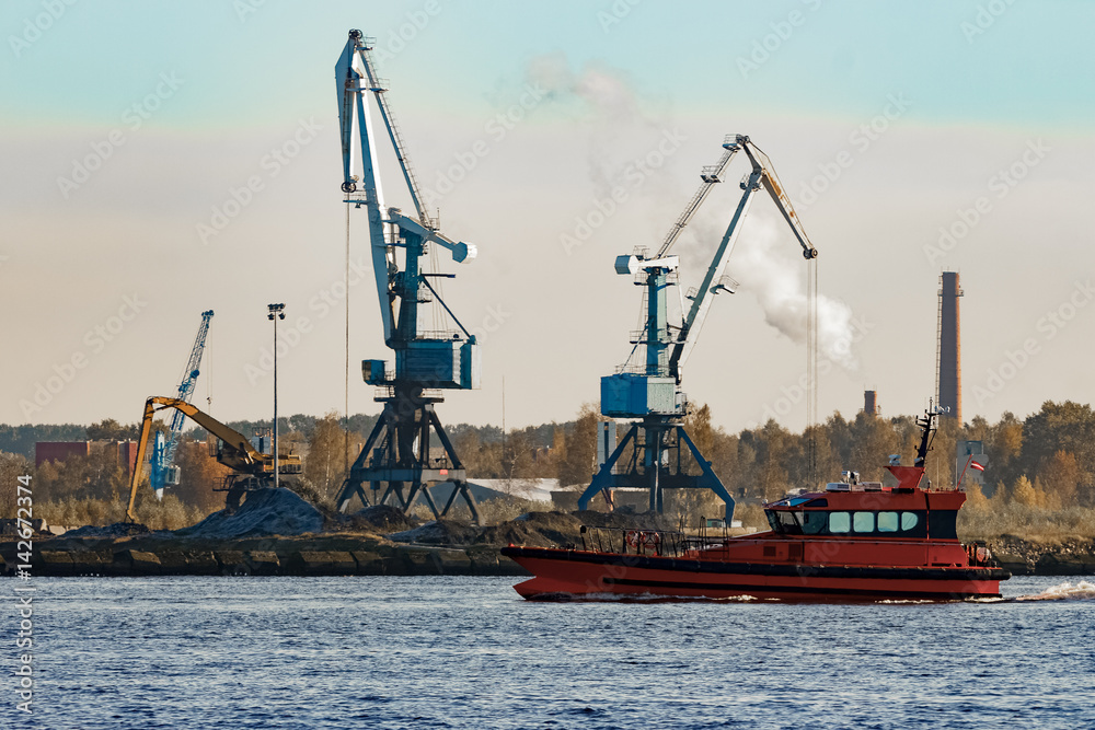 Orange pilot ship sailing against the cargo cranes Orange pilot ship sailing against the cargo cranes