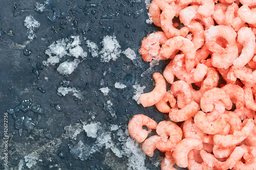 Frozen shrimp with ice cubes on a concrete background