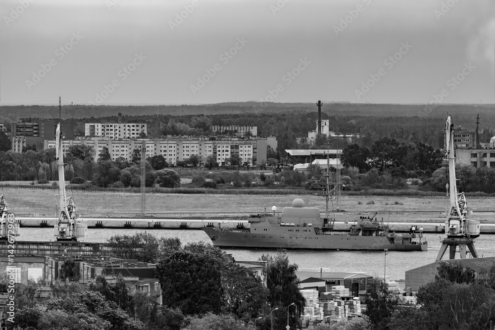 Military ship sailing past the cargo port in Riga, Latvia. Monoc