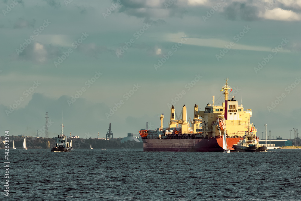 Red cargo ship and the tug ship towing  it to the port