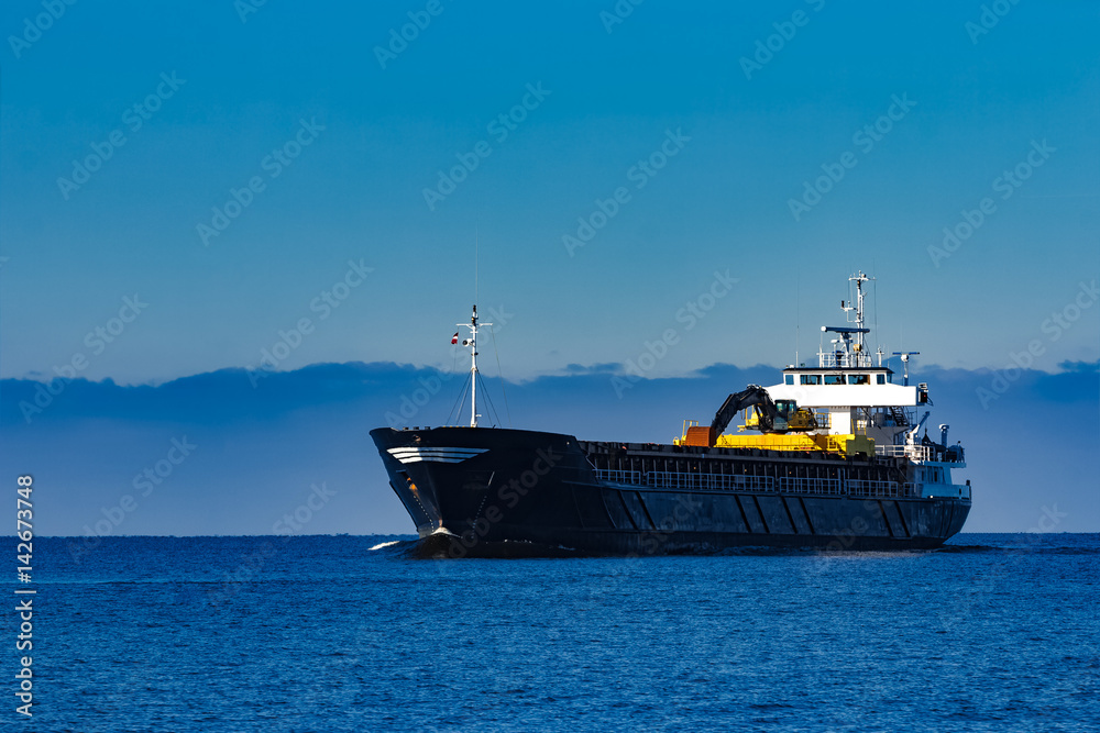 Black cargo ship with long reach excavator moving by baltic sea