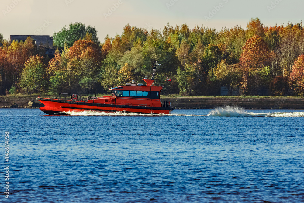 Fototapeta premium Red pilot ship moving past the autumn trees in Europe