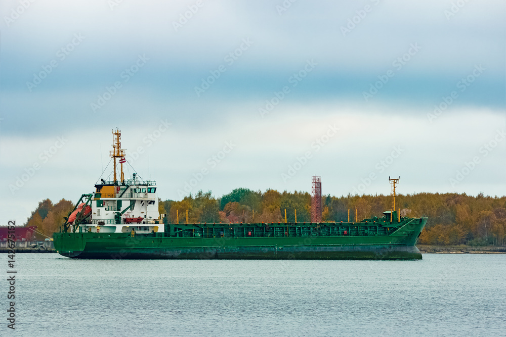 Green cargo ship moving to the port in cloudy day