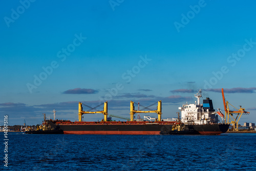 Black cargo ship mooring at the port with tug ship support