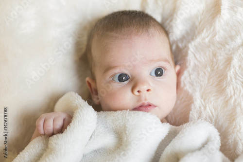 Portrait of a cute baby girl awake, looking at the camera. She is holding a white blanket. White background