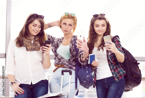 three young girls standing with luggage at the airport and looking at phone. A trip with friends