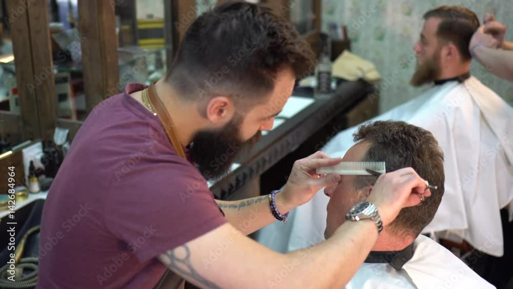 Two barbers cuts the hair of the clients with scissors, close up Two barbers cuts the hair of the clients with scissors, close up