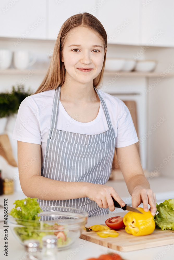 Cheerful teenage girl cooking healthy dinner in the kitchen