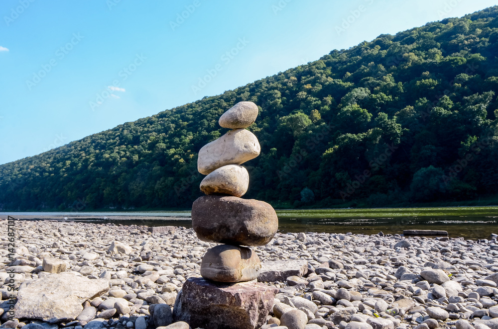 A pile of stones on the bank of the Buller River, with the river in the background and the surrounding high cliffs covered in bush