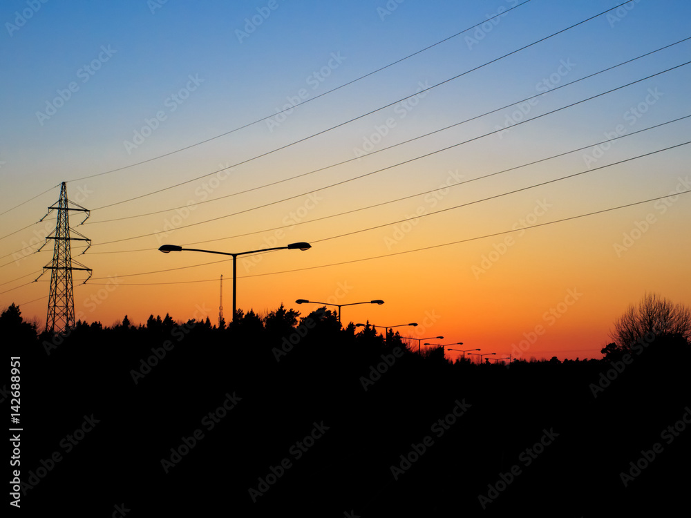 Sunset over silhouette urban landscape with power lines and light poles