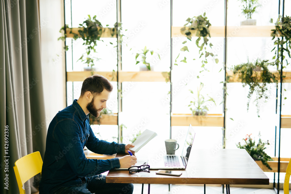 Freelance man working on line with a laptop and holding documents in a modern office Freelance man working on line with a laptop and holding documents in a modern office