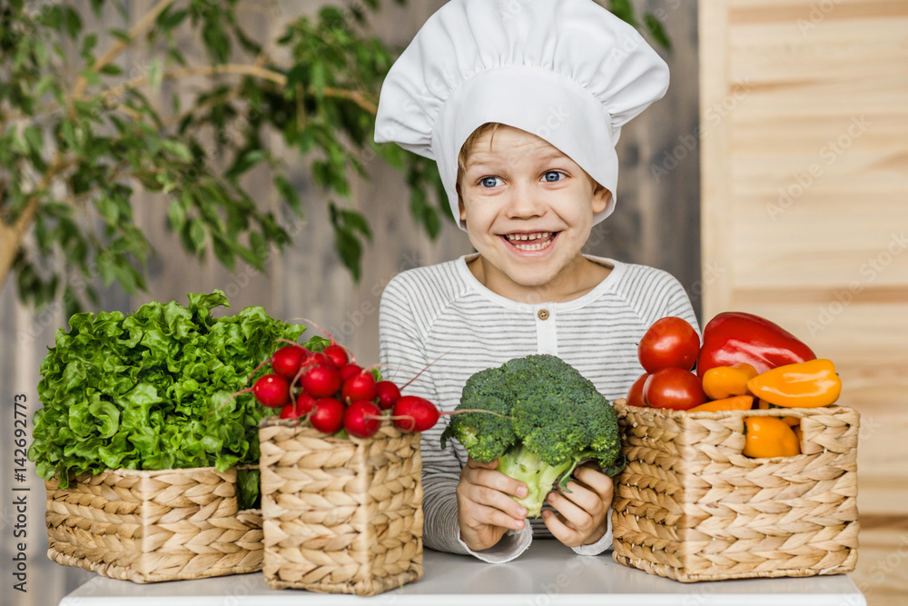 Cute boy in chef uniform with vegetables. Cooking in kitchen at home. Vegetarian. Healthy food Cute boy in chef uniform with vegetables. Cooking in kitchen at home. Vegetarian. Healthy food