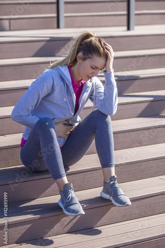 Young woman with abdominal pain after sitting on the steps of recreational running