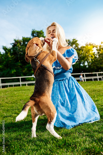 Young beautiful blonde girl walking  playing with beagle dog in park.