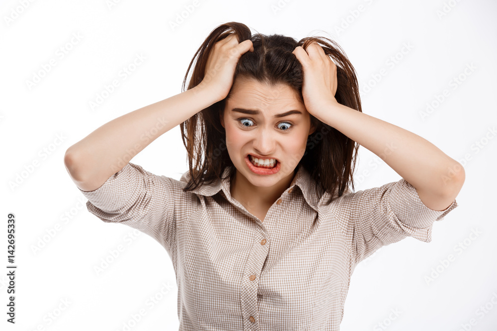 Young beautiful angry crazy brunette businessgirl clutching her head and screaming looking away over white background Young beautiful angry crazy brunette businessgirl clutching her head and screaming looking away over white background