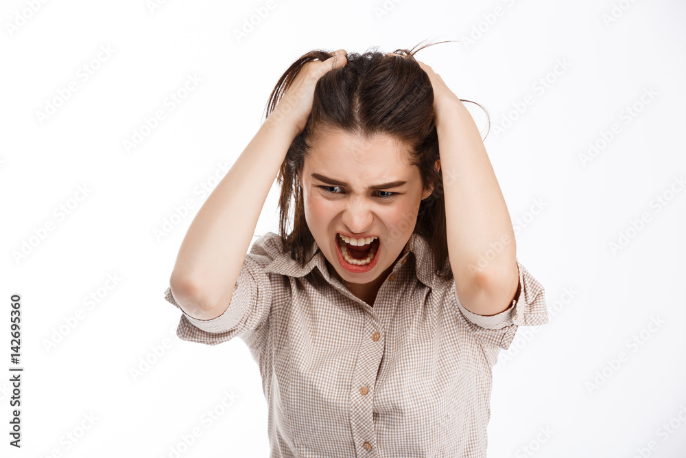 Young beautiful angry crazy brunette businessgirl clutching her head and screaming looking down over white background Young beautiful angry crazy brunette businessgirl clutching her head and screaming looking down over white background