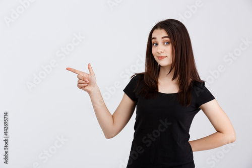 Young beautiful girl in black t-shirt pointing fingers in side over white background 