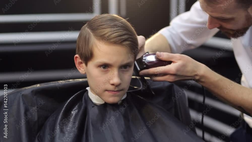 A bearded barber is cutting a little boy, close-up. A bearded barber is cutting a little boy, close-up.