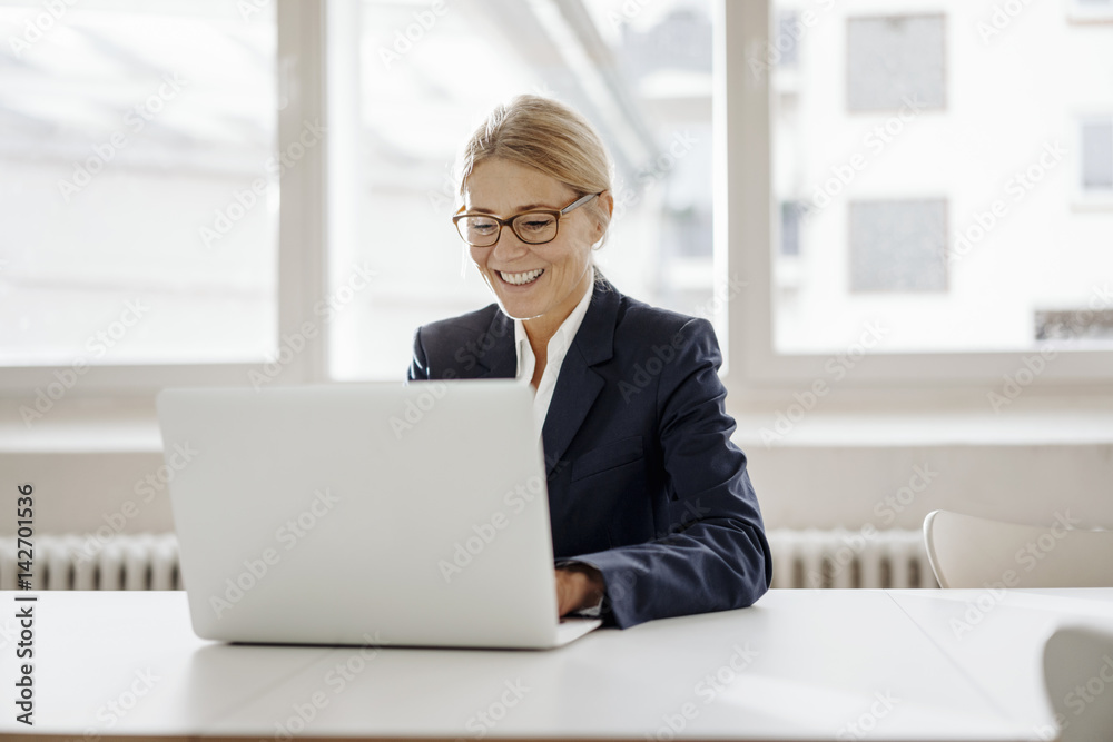 Smiling businesswoman using laptop in office Smiling businesswoman using laptop in office