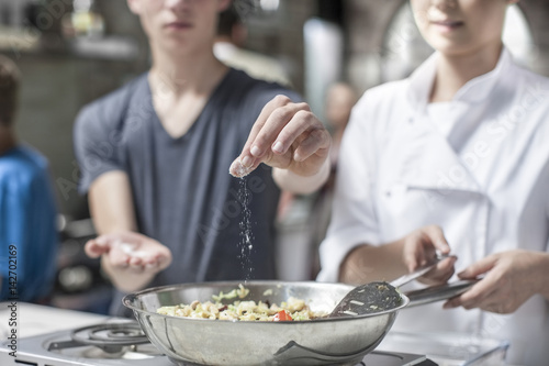 Teenager adding salt to pan