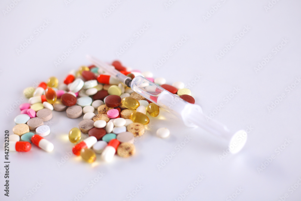 Tablets and a syringe lying on a white table Tablets and a syringe lying on a white table