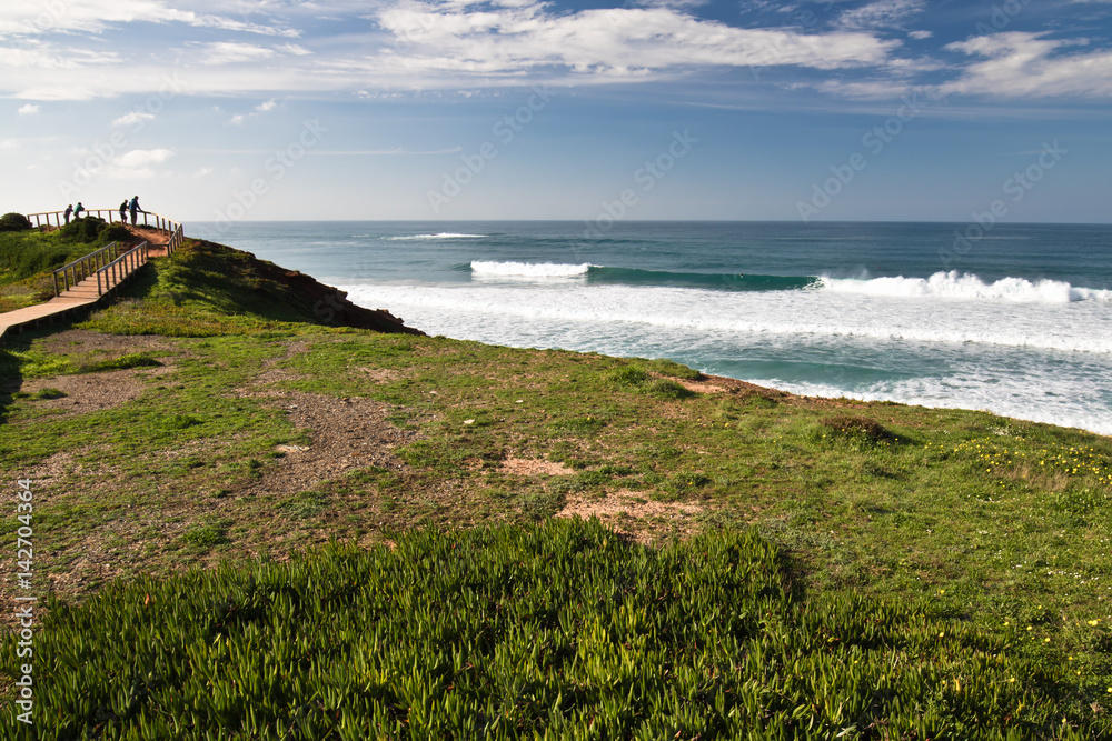 people admiring waves and surfers on surf spot on amado beach in vivid colors, algarve, portugal