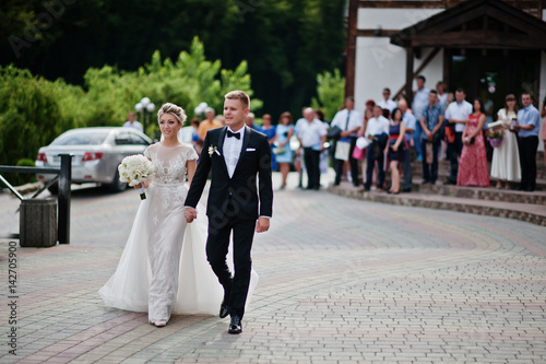 Groom with bride walking to the restaurant against guests at wedding day.