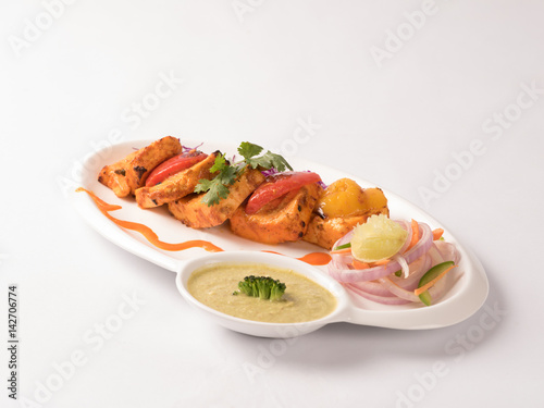 Paneer tikka with mint yogurt chutney served in a white plate on white background
