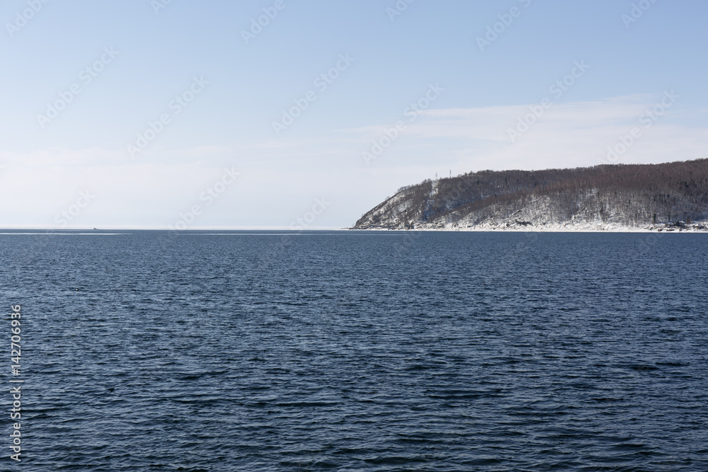 Baikal lake spring landscape view. Snow-covered shore of the lake. Rocky forested coastline. Baikal lake spring landscape view. Snow-covered shore of the lake. Rocky forested coastline.
