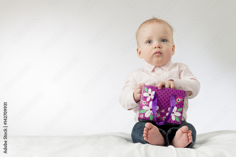 Serious baby boy holding some present in his arms. Thoughtful infant kid with a gift. Copy space. Ready postcard Serious baby boy holding some present in his arms. Thoughtful infant kid with a gift. Copy space. Ready postcard