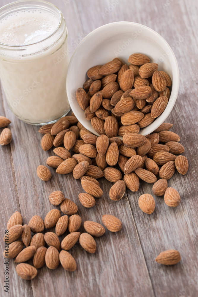White Bowl With Almonds Spilling and Glass of Almond Milk White Bowl With Almonds Spilling and Glass of Almond Milk