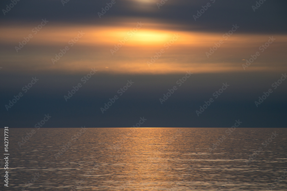 Sunset over horizon on tranquil water surface. Golden sunlight reflecting in water at the beach in late evening.
