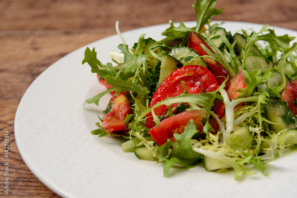 Vegetable salad in white round plate on wooden table. Macro.