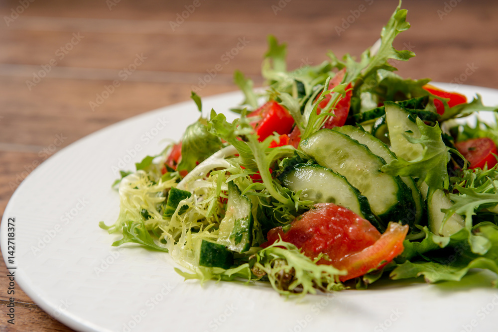 Vegetable salad in white round plate on wooden table. Macro.