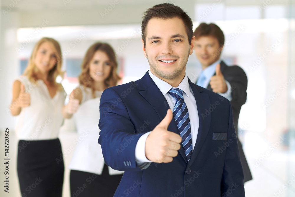 Successful young business people showing thumbs up sign while standing in office interier