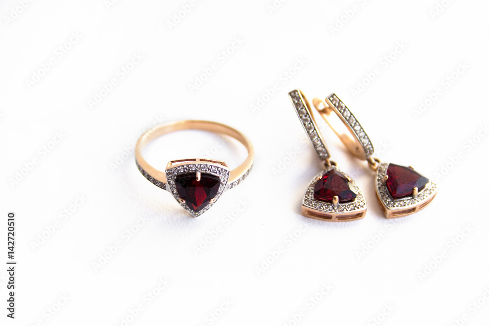 Gold ring and earrings with a red precious stone and small diamonds on a white background. Gold ring and earrings with a red precious stone and small diamonds on a white background.