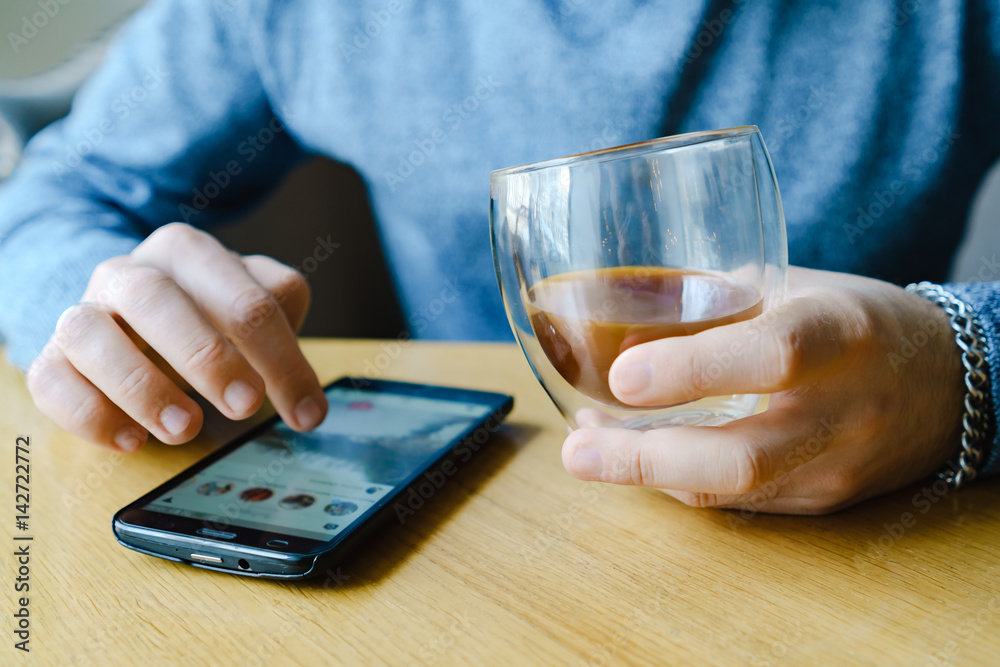 Male hand with coffee in glass and smartphone in cafe