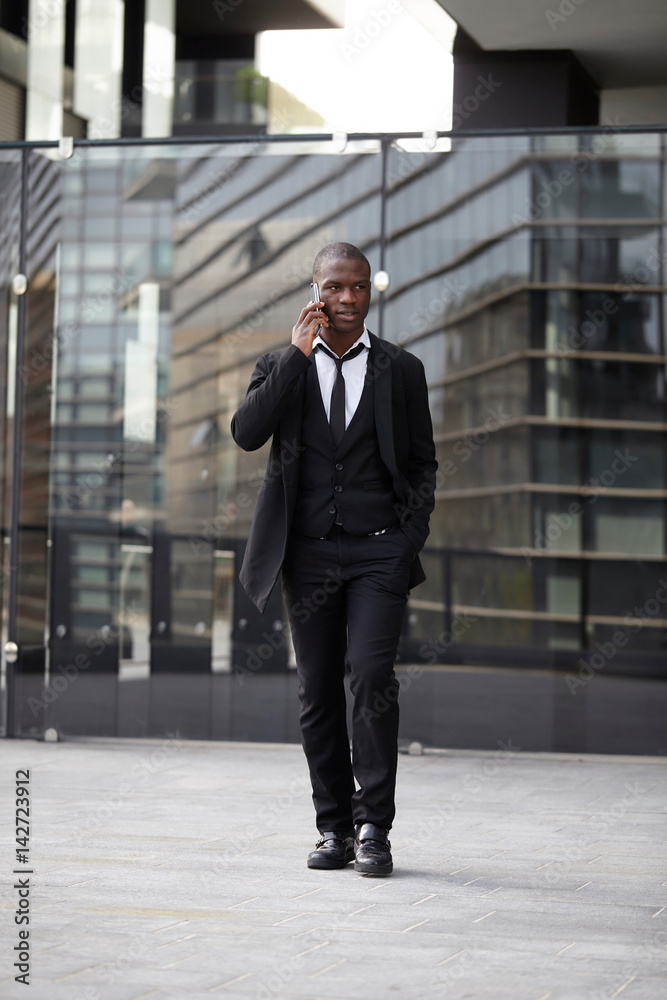 Full length portrait of a confident young businessman walking in the city talking on cell phone Full length portrait of a confident young businessman walking in the city talking on cell phone