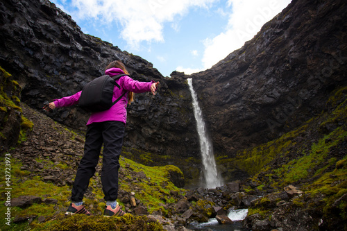 Happy woman by waterfall with arms raised. Back view. Iceland.