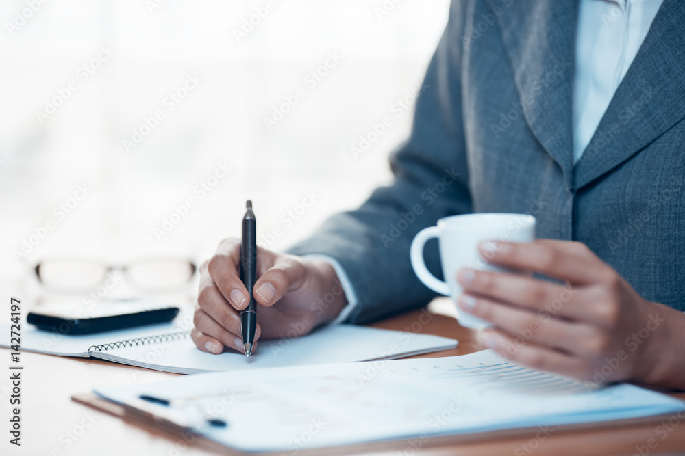 Businesswoman writing report in office and drink coffee Businesswoman writing report in office and drink coffee