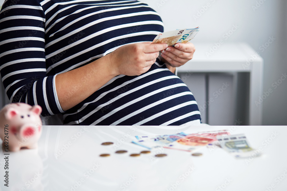 Obraz premium Pregnant woman behind the desk in the office counting money