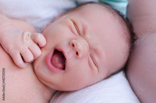 Cute yawning newborn baby boy resting on the bed